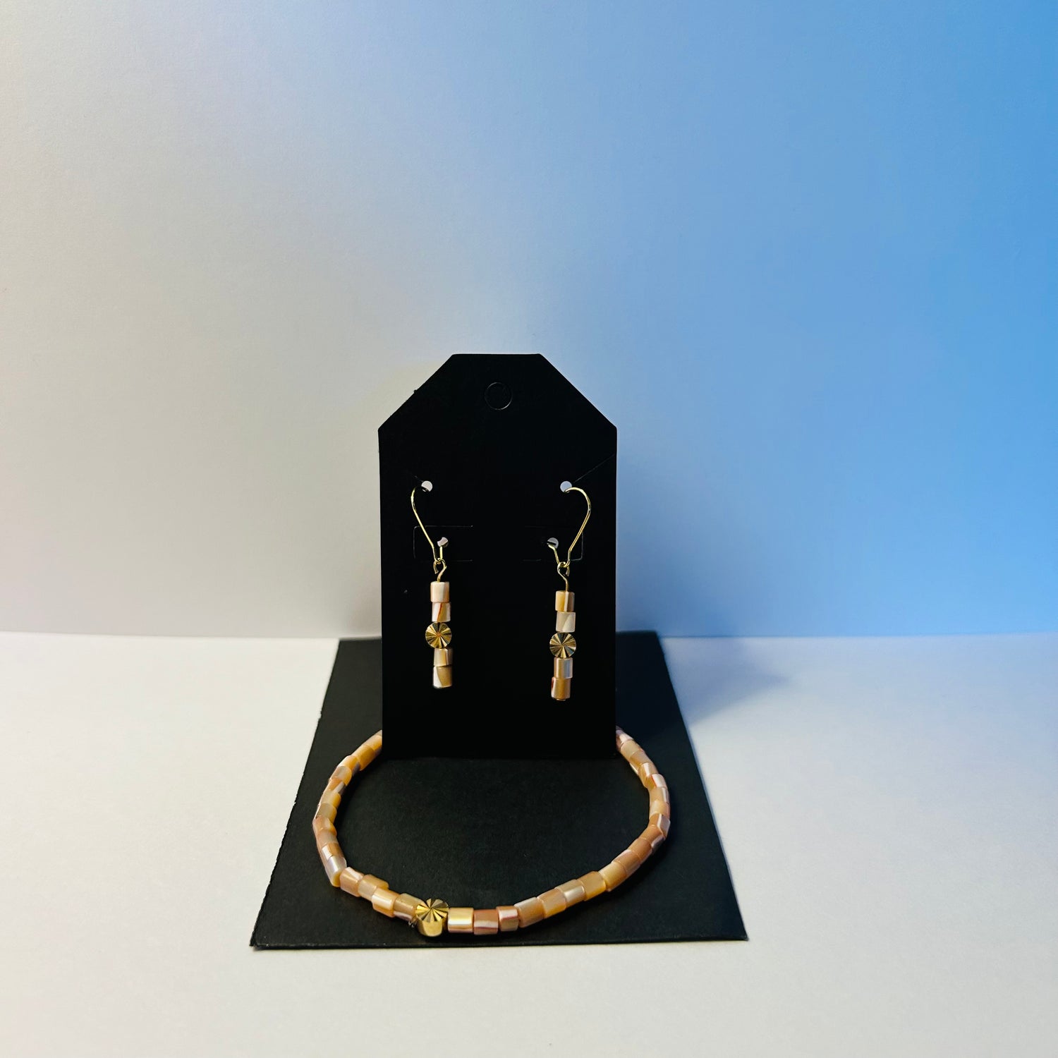 Jewelry set with bracelet and earrings on a black stand against a gradient background