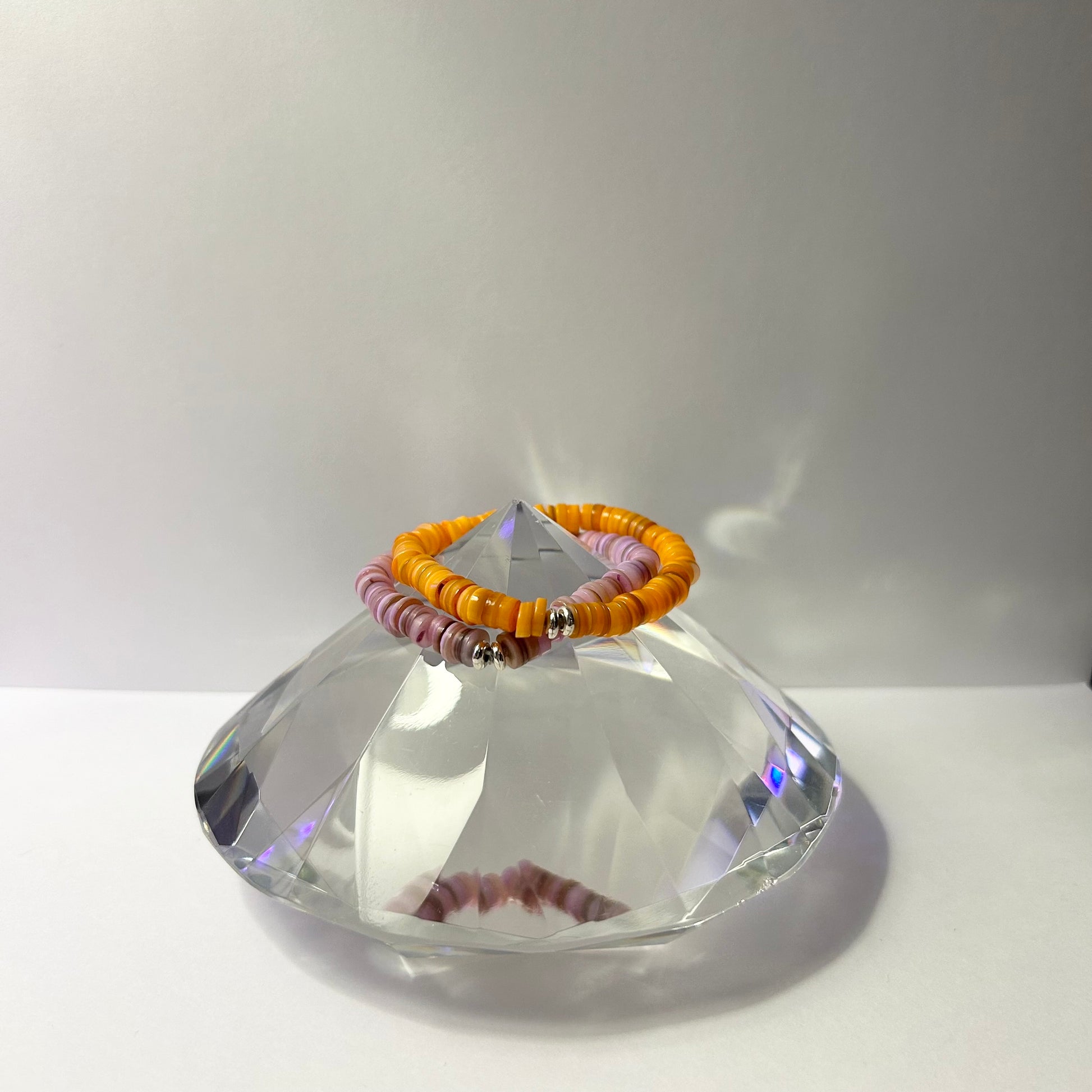 Two bracelets on a clear crystal stand against a white background