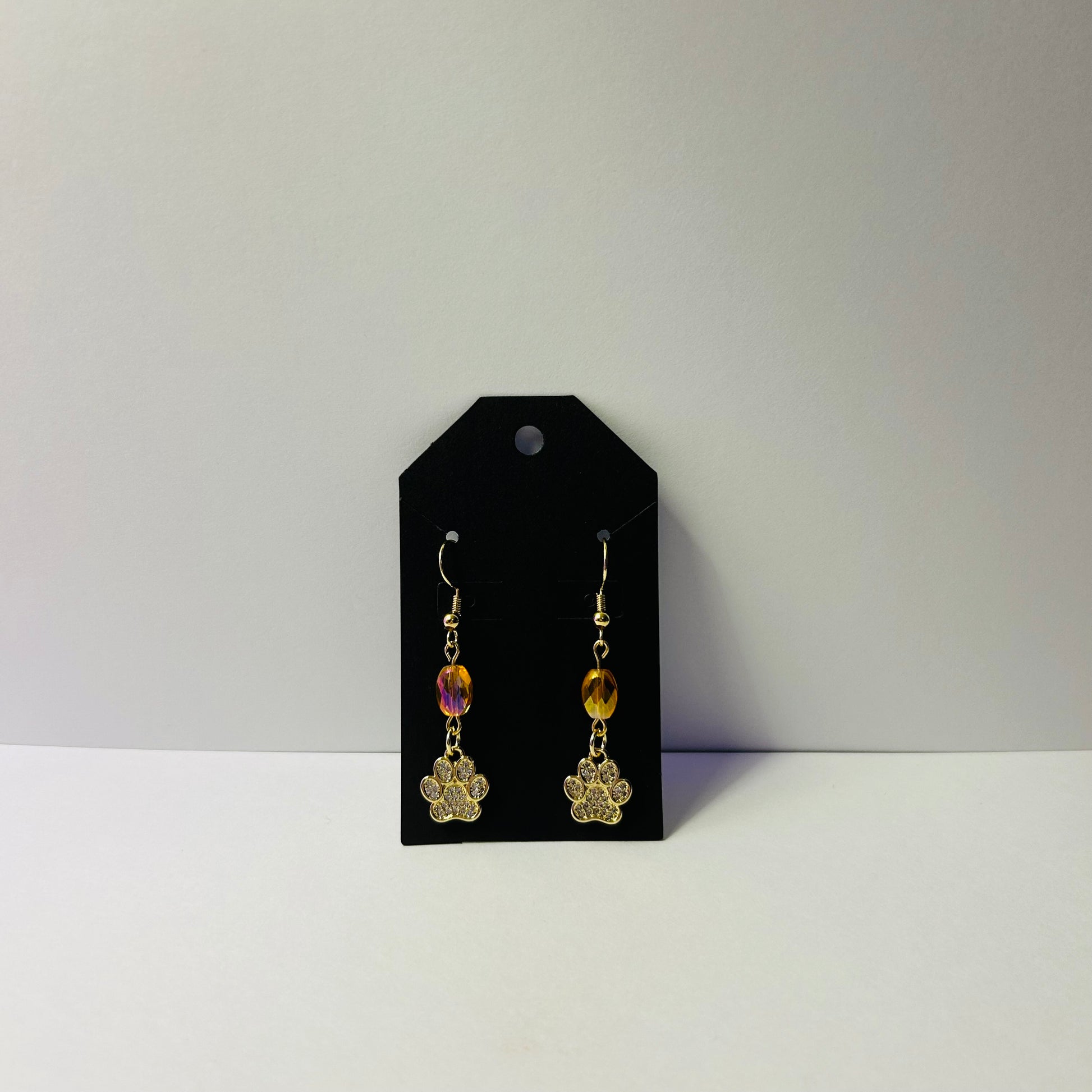 Gold earrings with colorful beads on a black card against a gray background