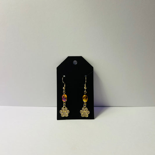Gold earrings with colorful beads on a black card against a gray background