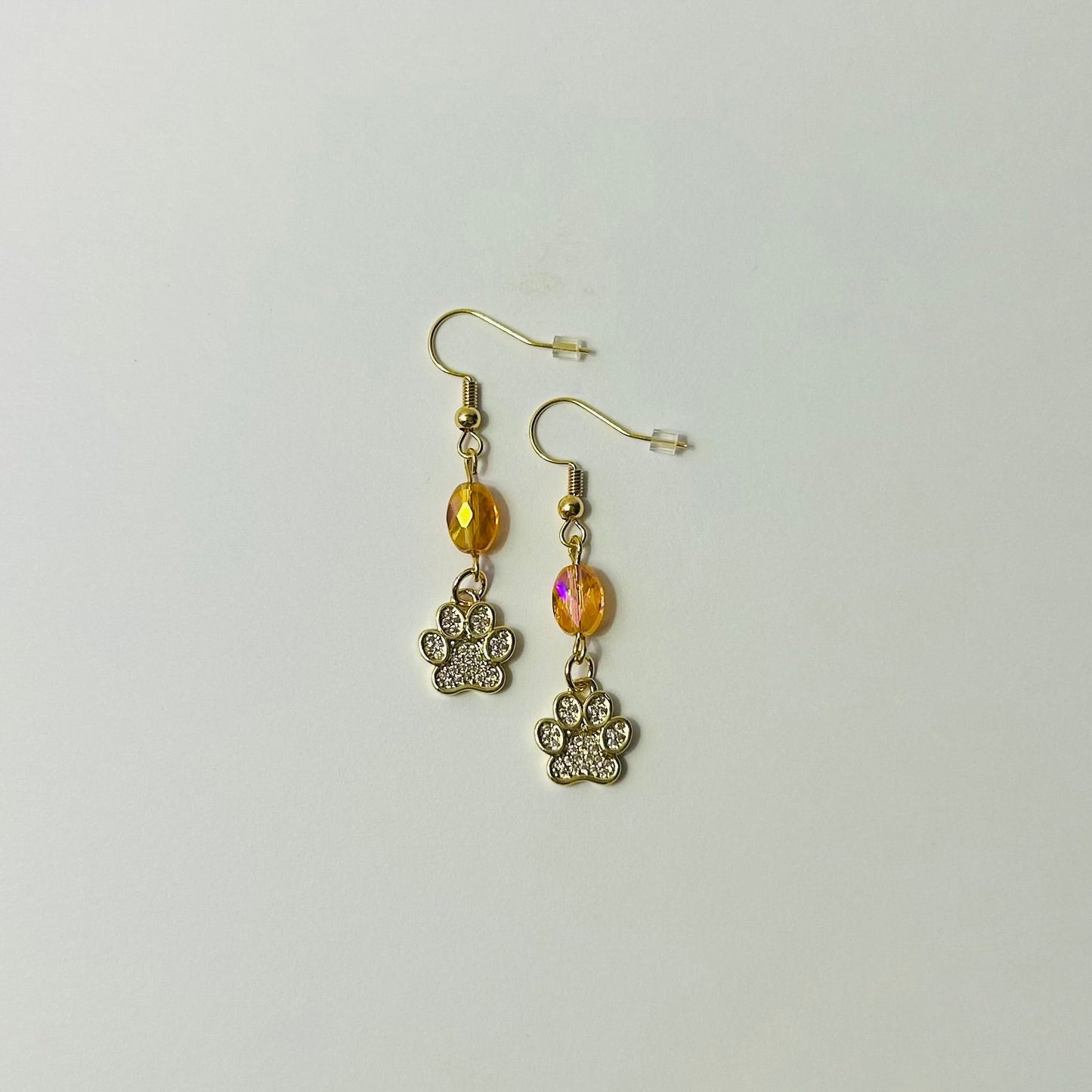 Pair of earrings with paw charm and yellow gemstone on a light gray background