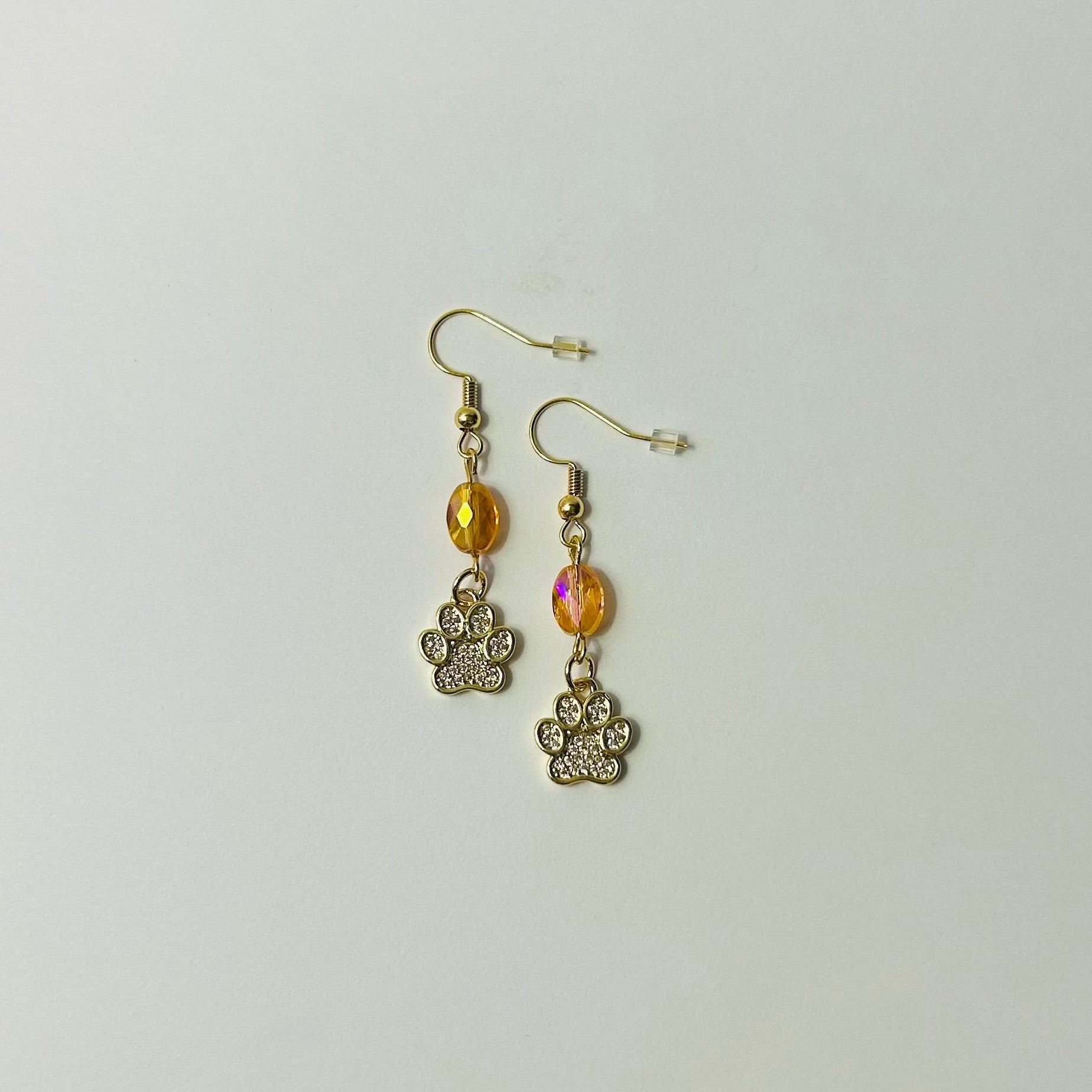 Pair of earrings with paw charm and yellow gemstone on a light gray background