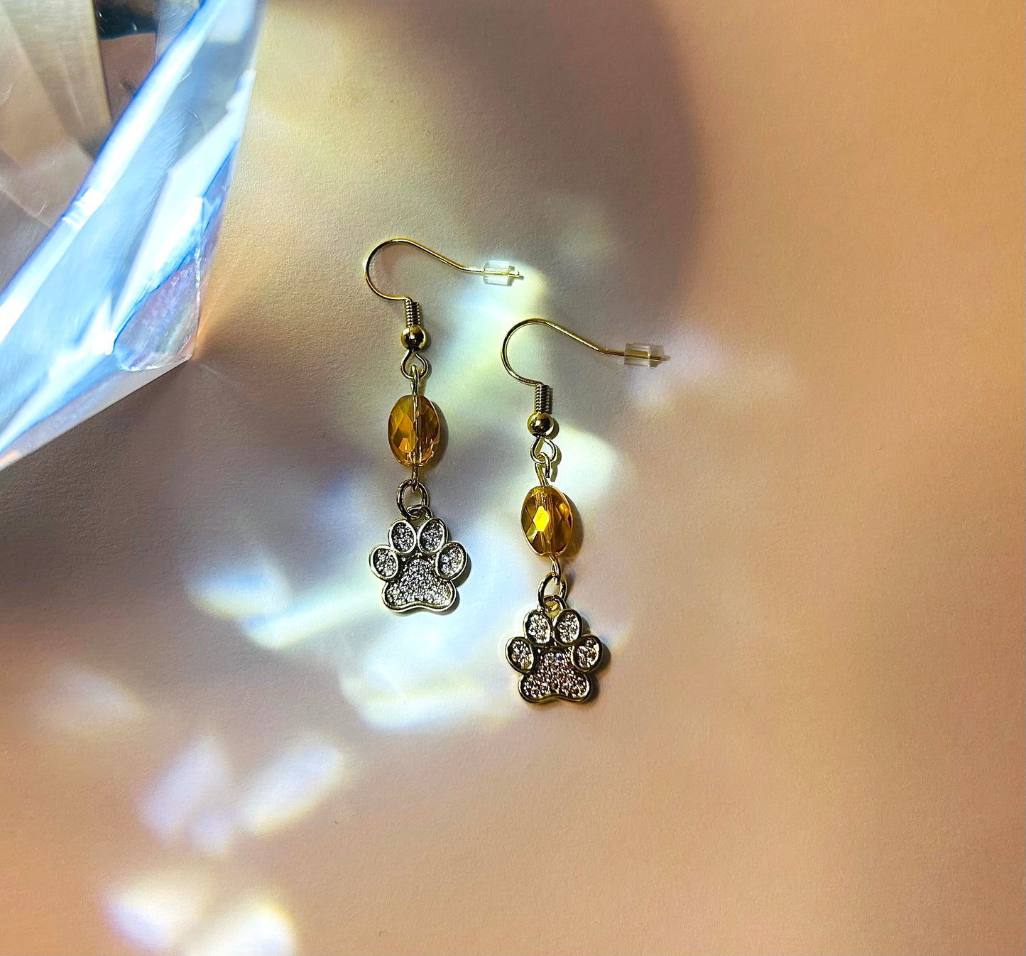 Pair of earrings with paw charm and orange bead on a neutral background